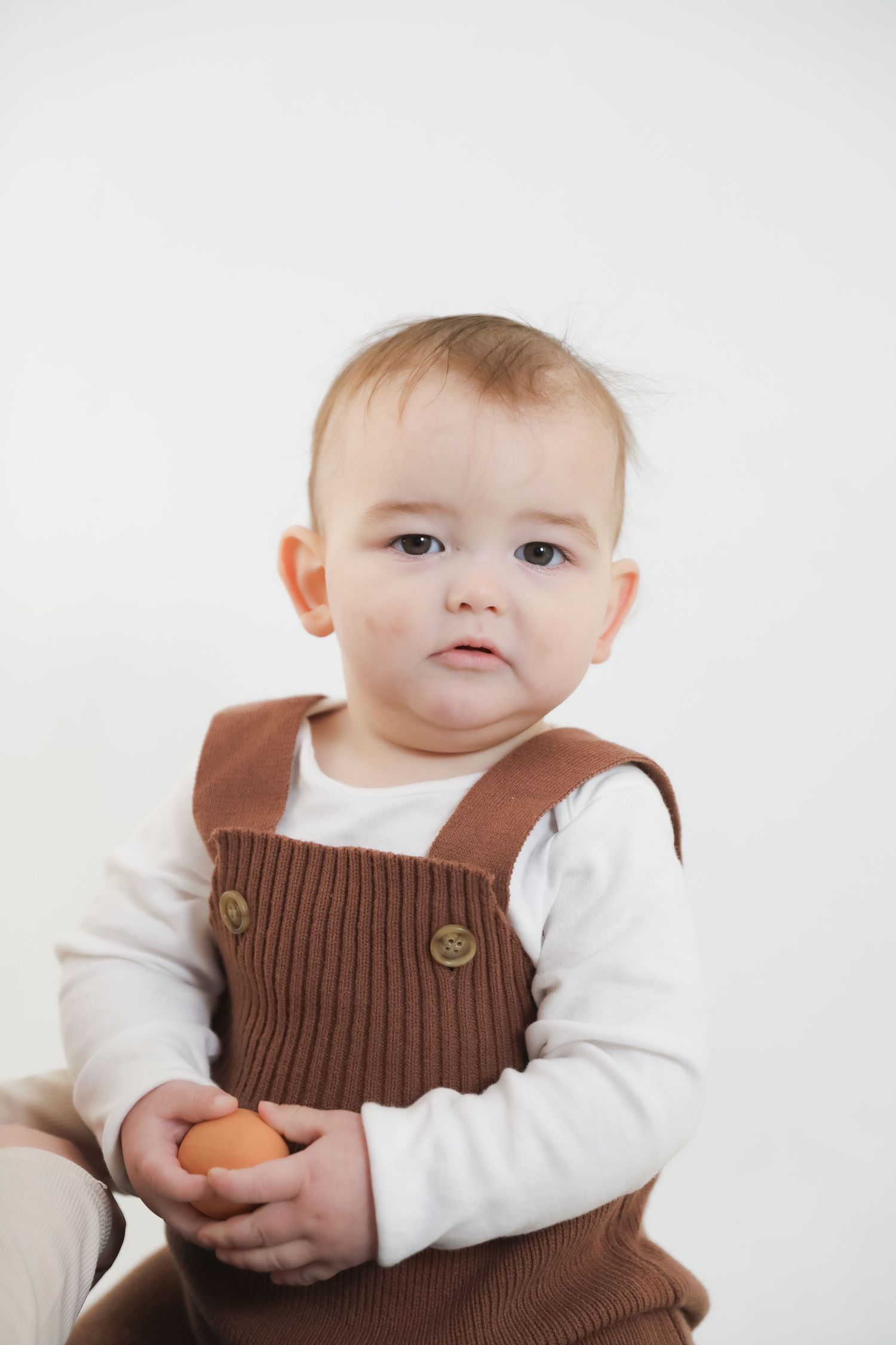 Adorable baby wearing a brown knit vest and white shirt poses for a series of sweet portraits.