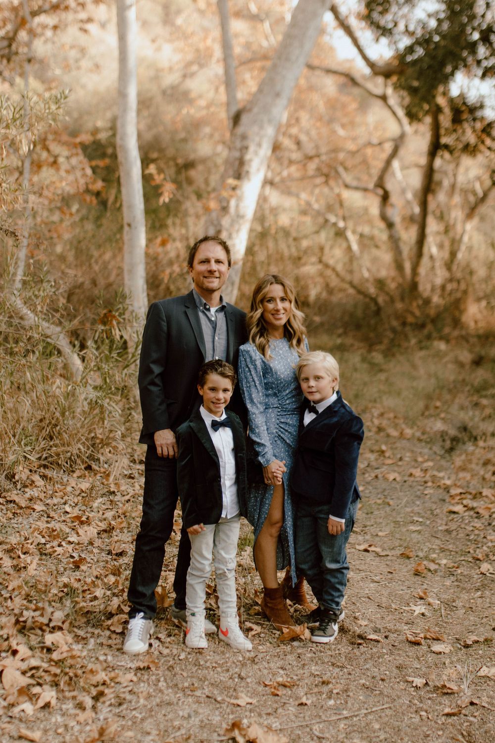 A family stands together on a wooded trail during autumn with tall white trees in the background.