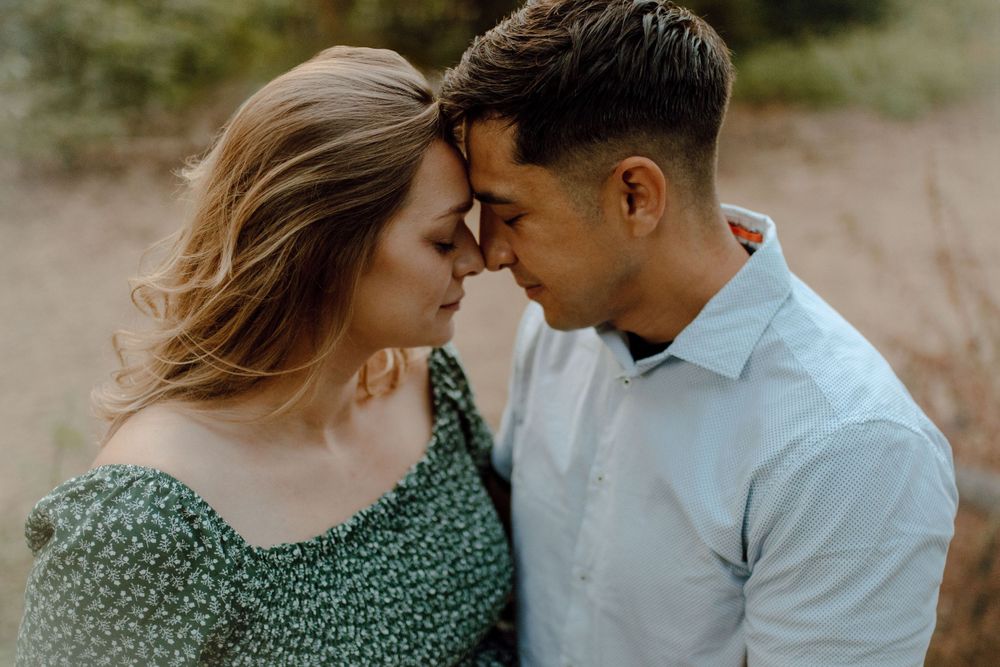 Intimate romantic portrait of a couple sharing a tender forehead touching moment outdoors during golden hour.