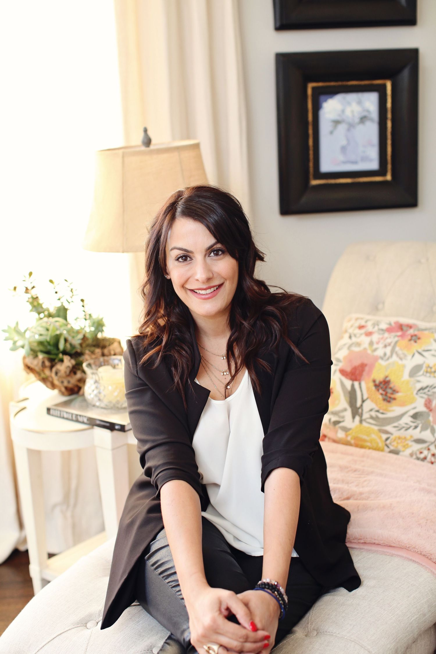 Portrait of woman in black blazer sitting casually on white couch in stylish living room.