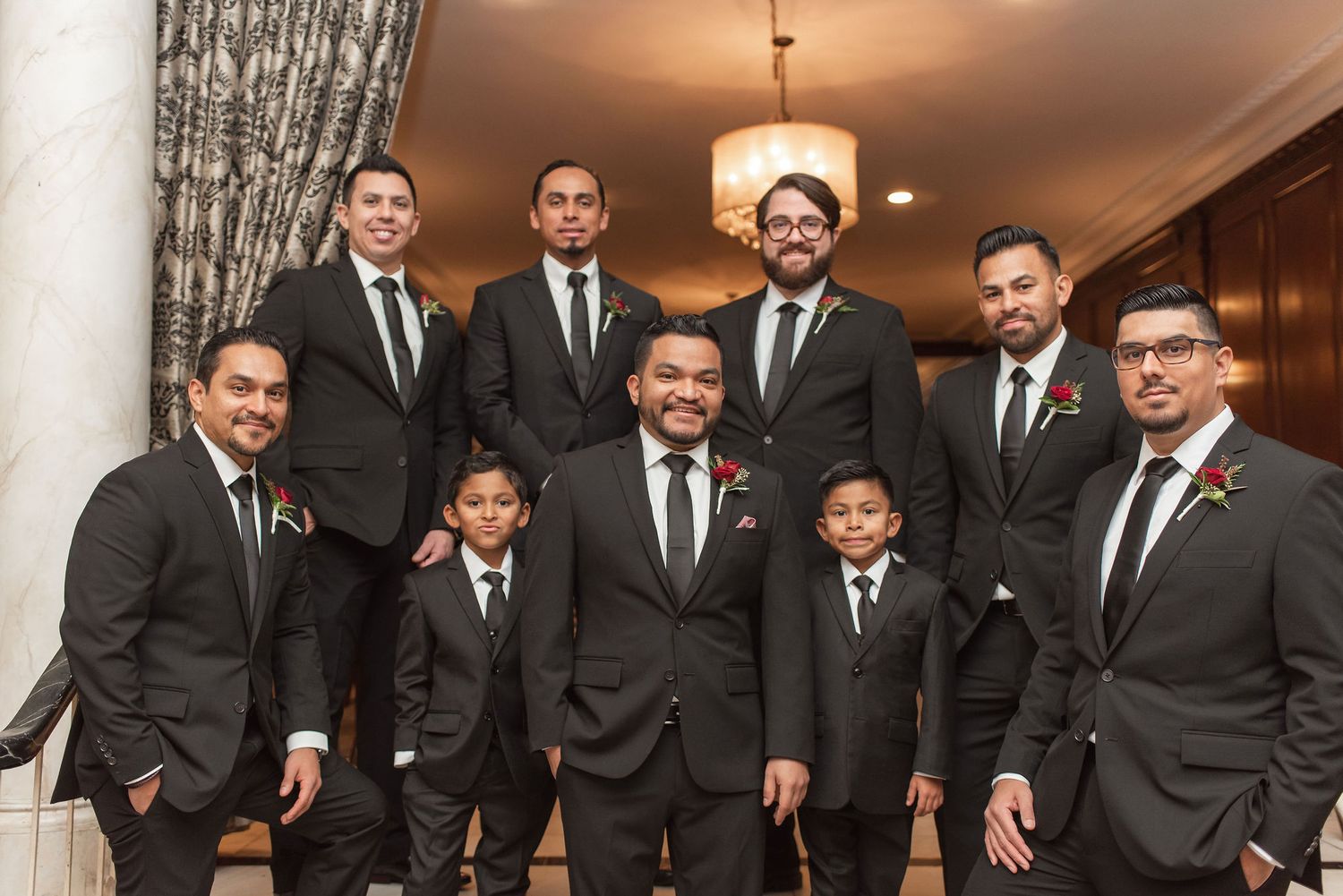 Groomsmen in black suits and ties gather for formal wedding portrait.