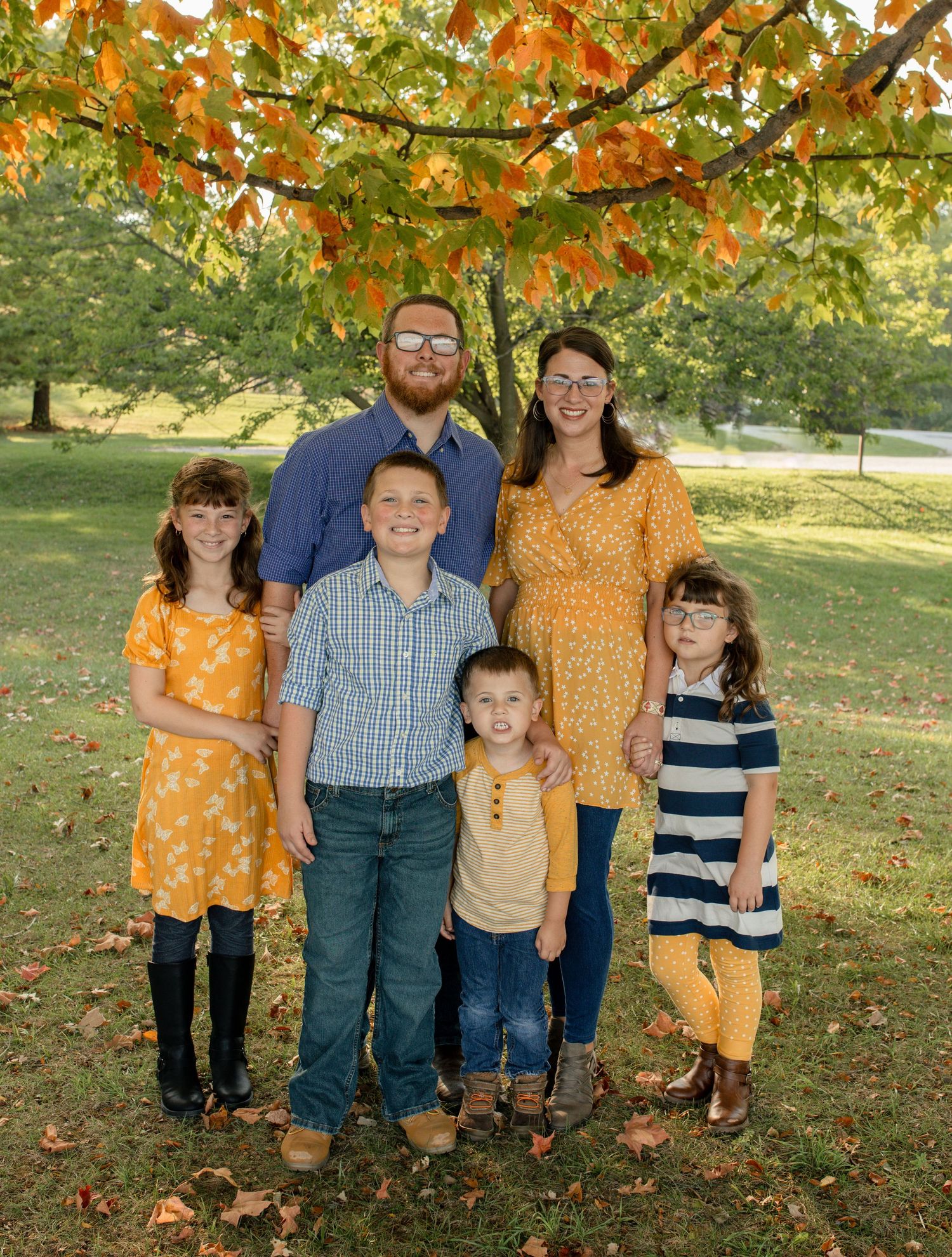 Family group portrait under autumn trees wearing coordinated orange and blue outfits.