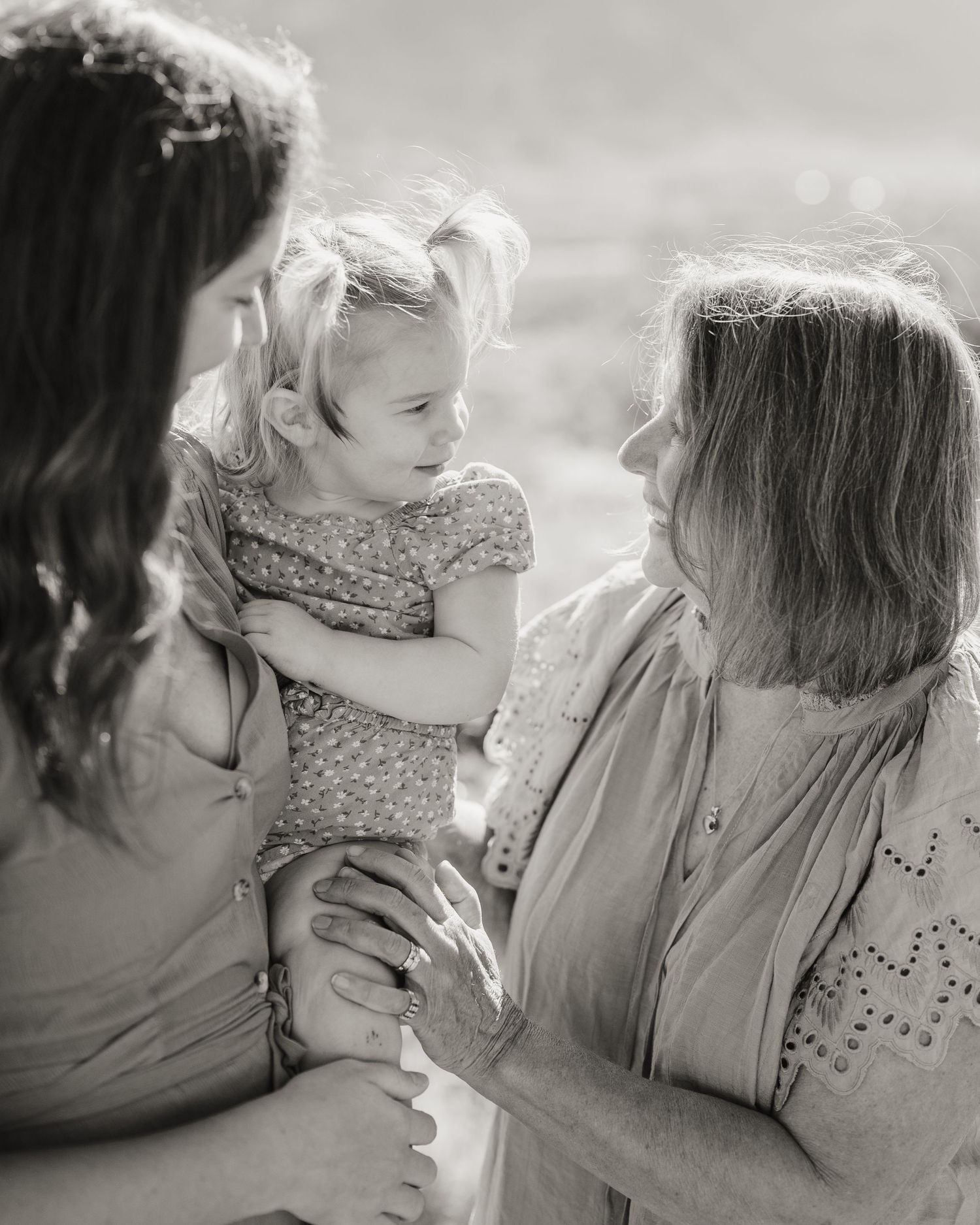 A black and white portrait of three generations sharing a tender moment outdoors.
