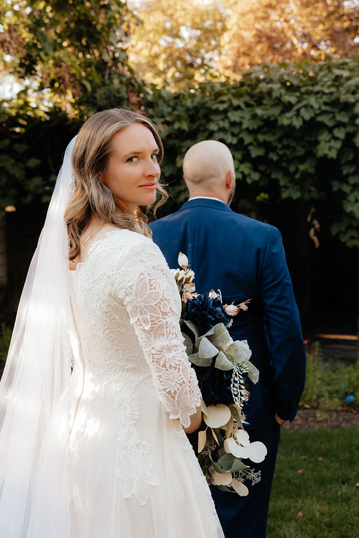 Bride standing behind groom looking over her shoulder at camera