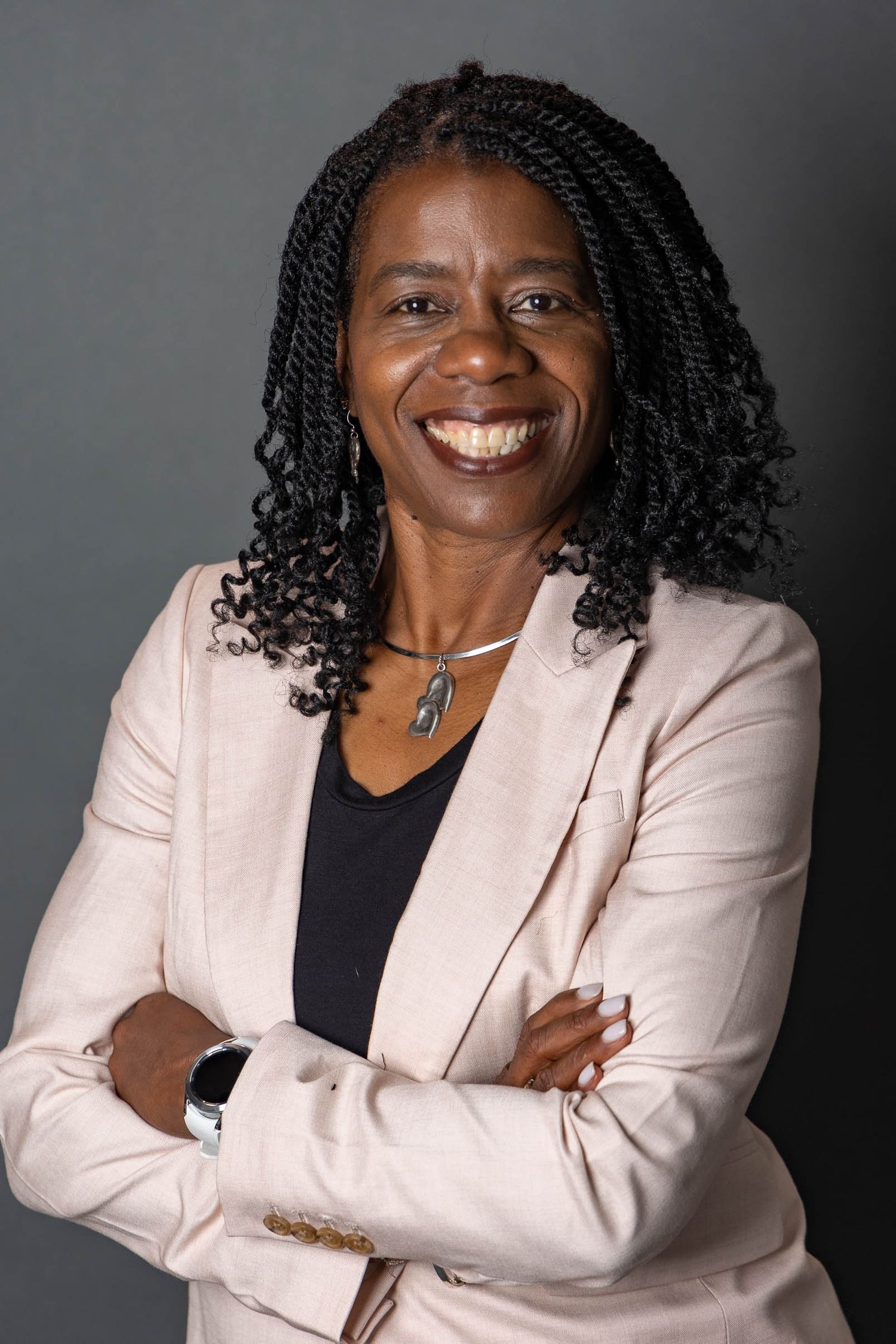 Professional headshot of a person in a light pink blazer and black top against a dark backdrop.