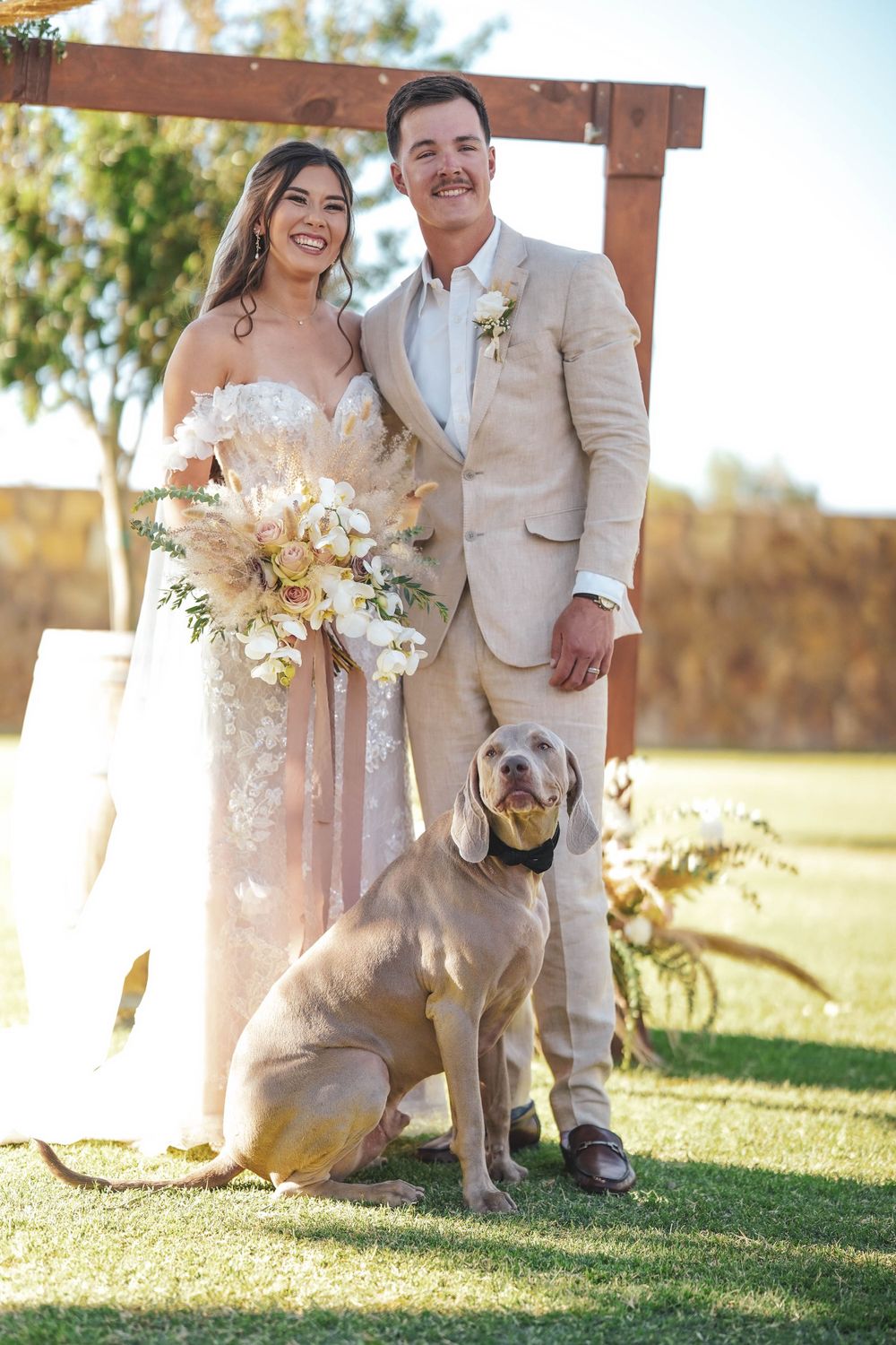 Newlyweds take photos with their pet dog during rustic outdoor wedding.