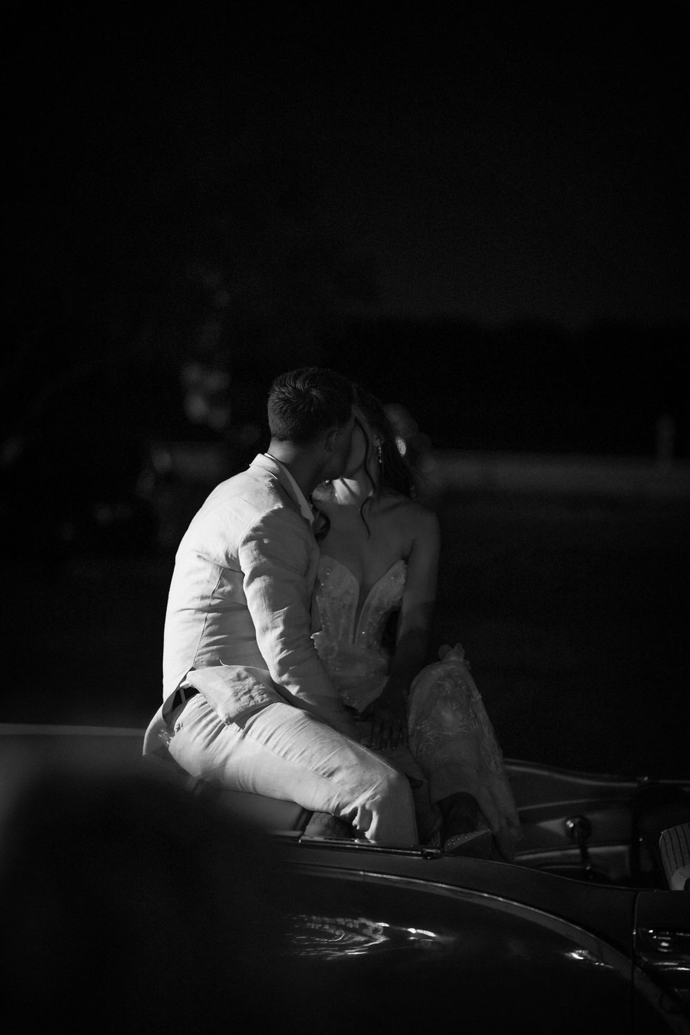 Monochrome image of couple in white attire sitting together at nighttime event.