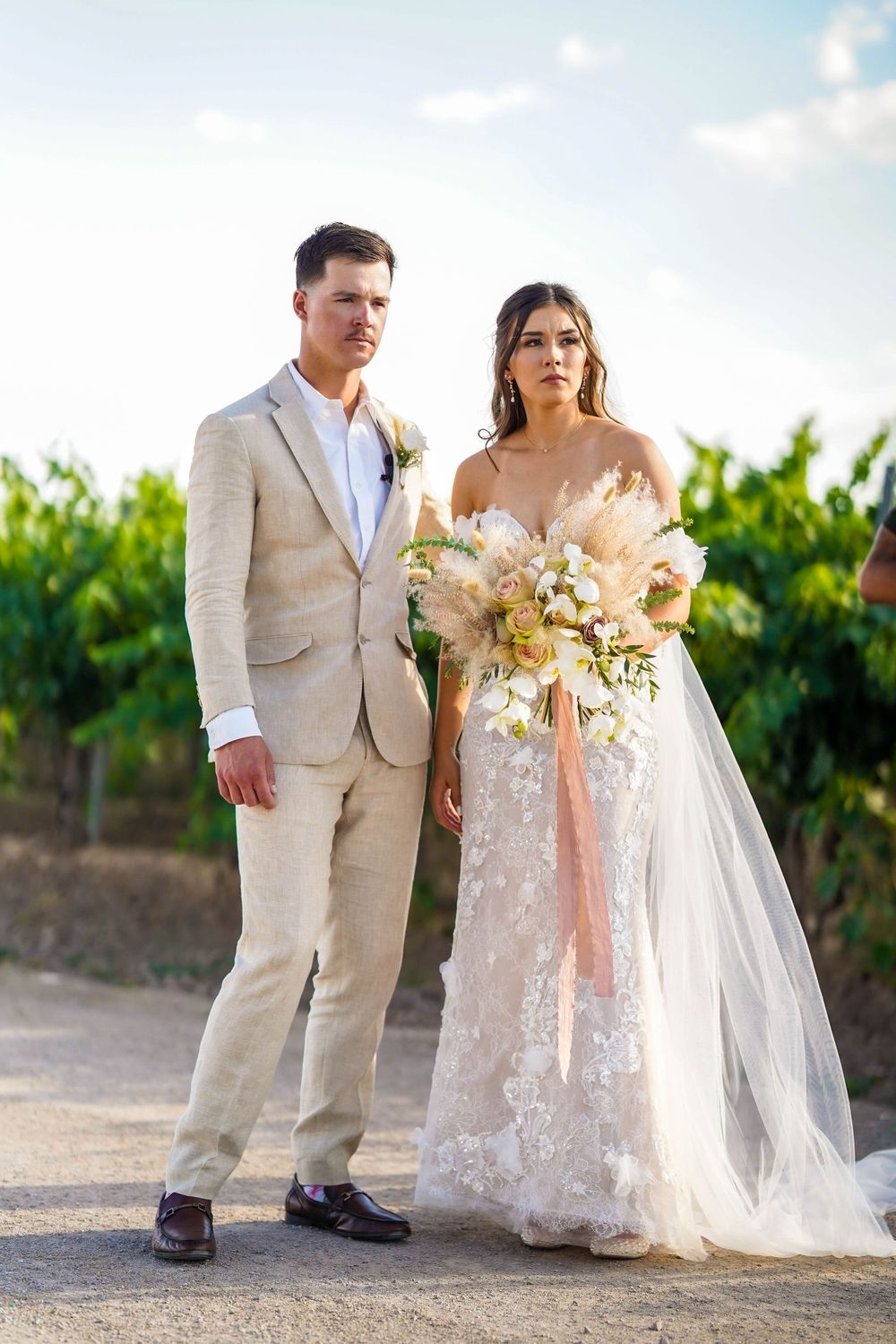 Newlyweds walking together through vineyard in elegant wedding attire.