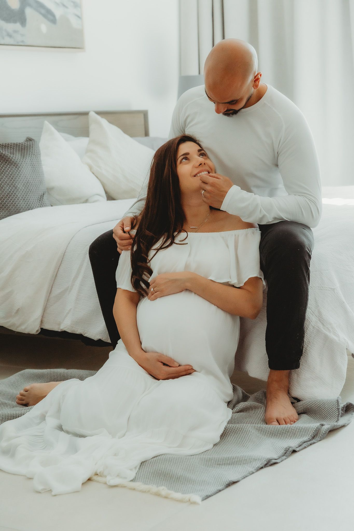 Expecting couple  sitting by the bed looking at each other and smiling