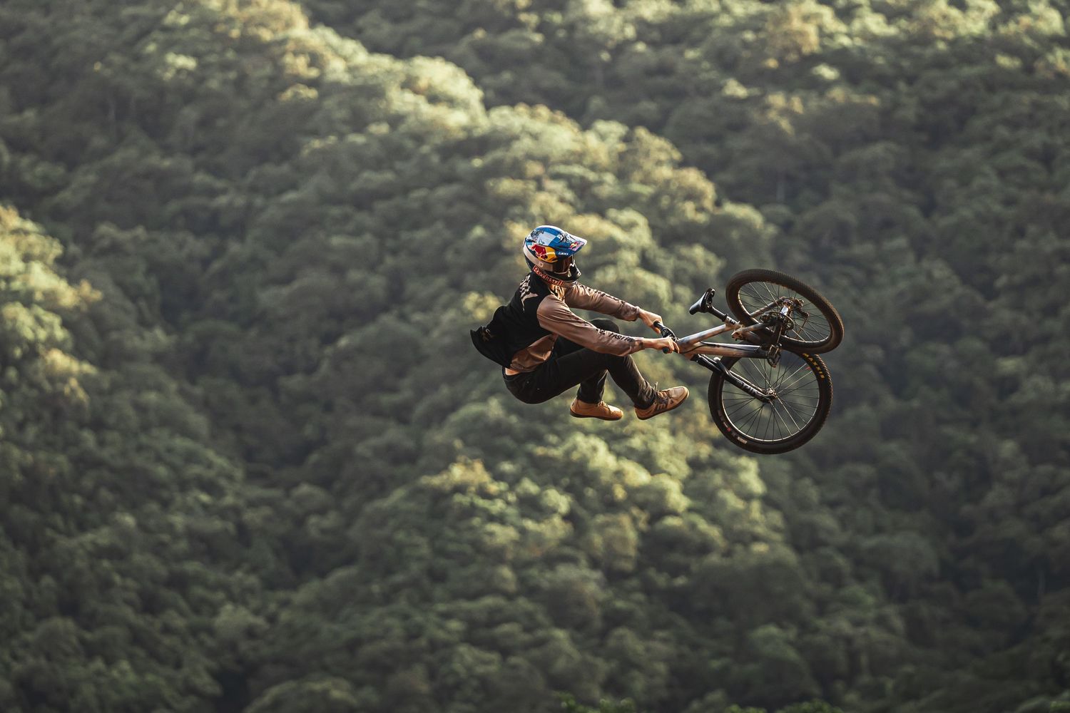 Mountain biker performing aerial tricks against forest backdrop.