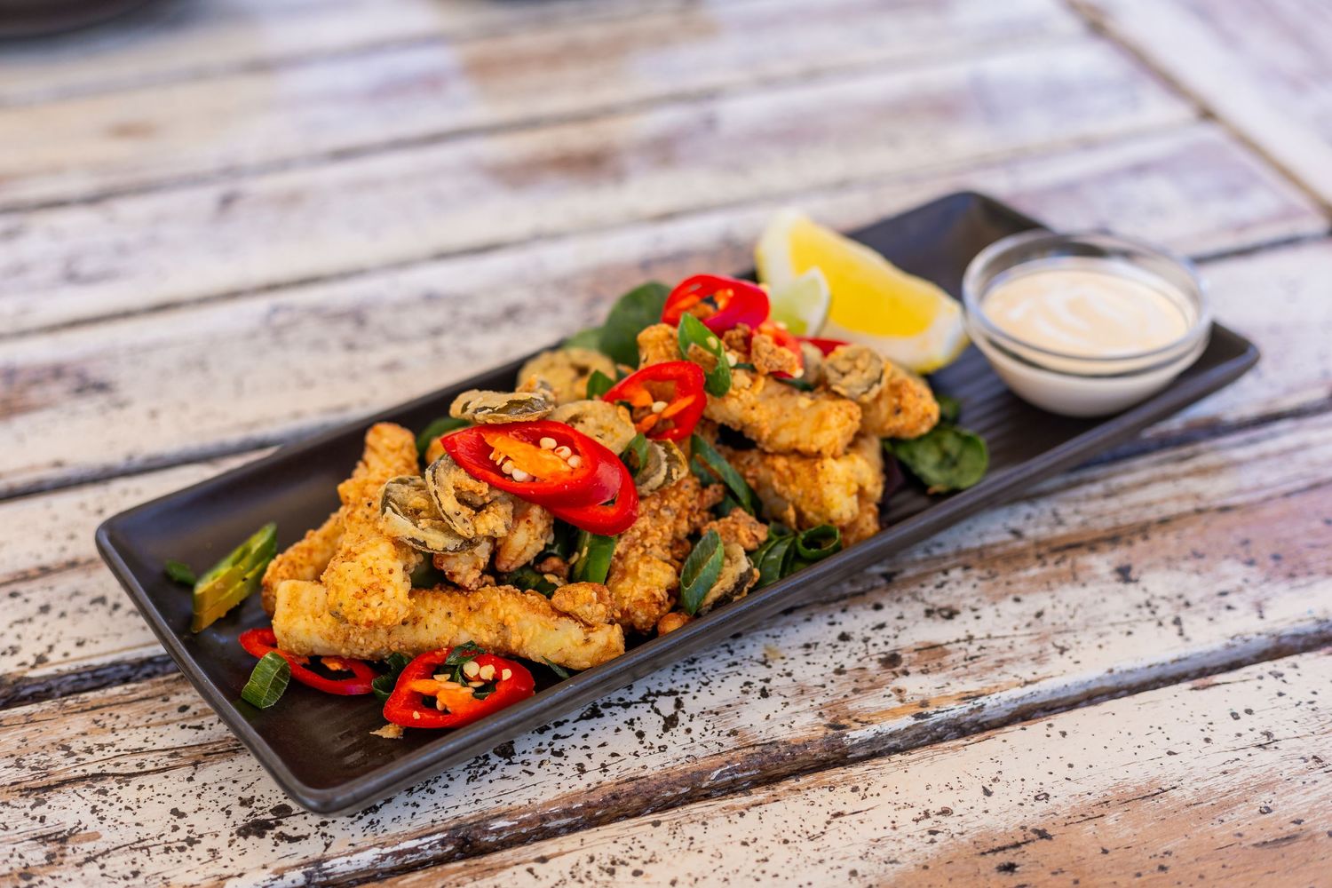 Spicy grilled chicken with red peppers and lemon served on black platter with dipping sauce.