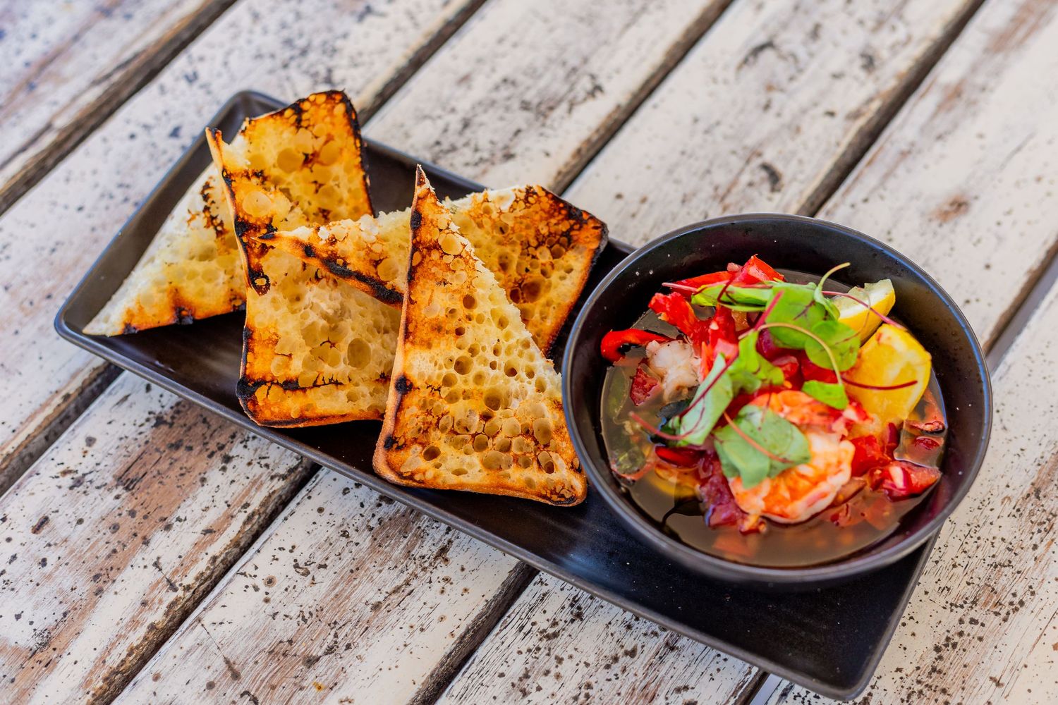 Grilled flatbread served with colorful salsa dip on dark plate.