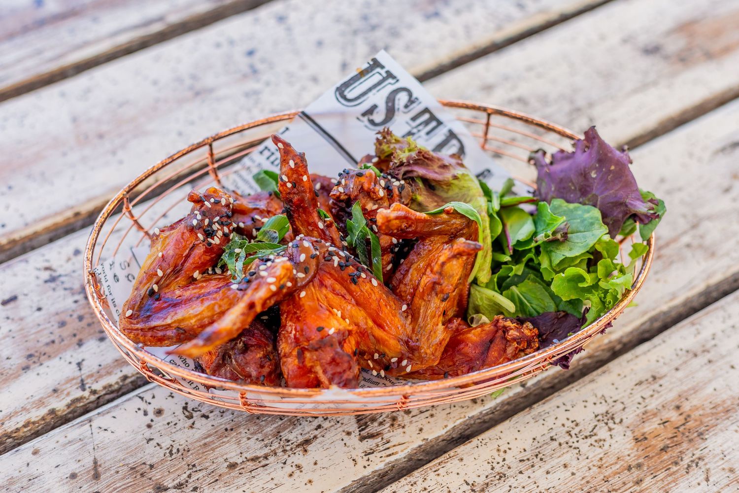 Spicy glazed wings garnished with fresh herbs in copper serving basket.
