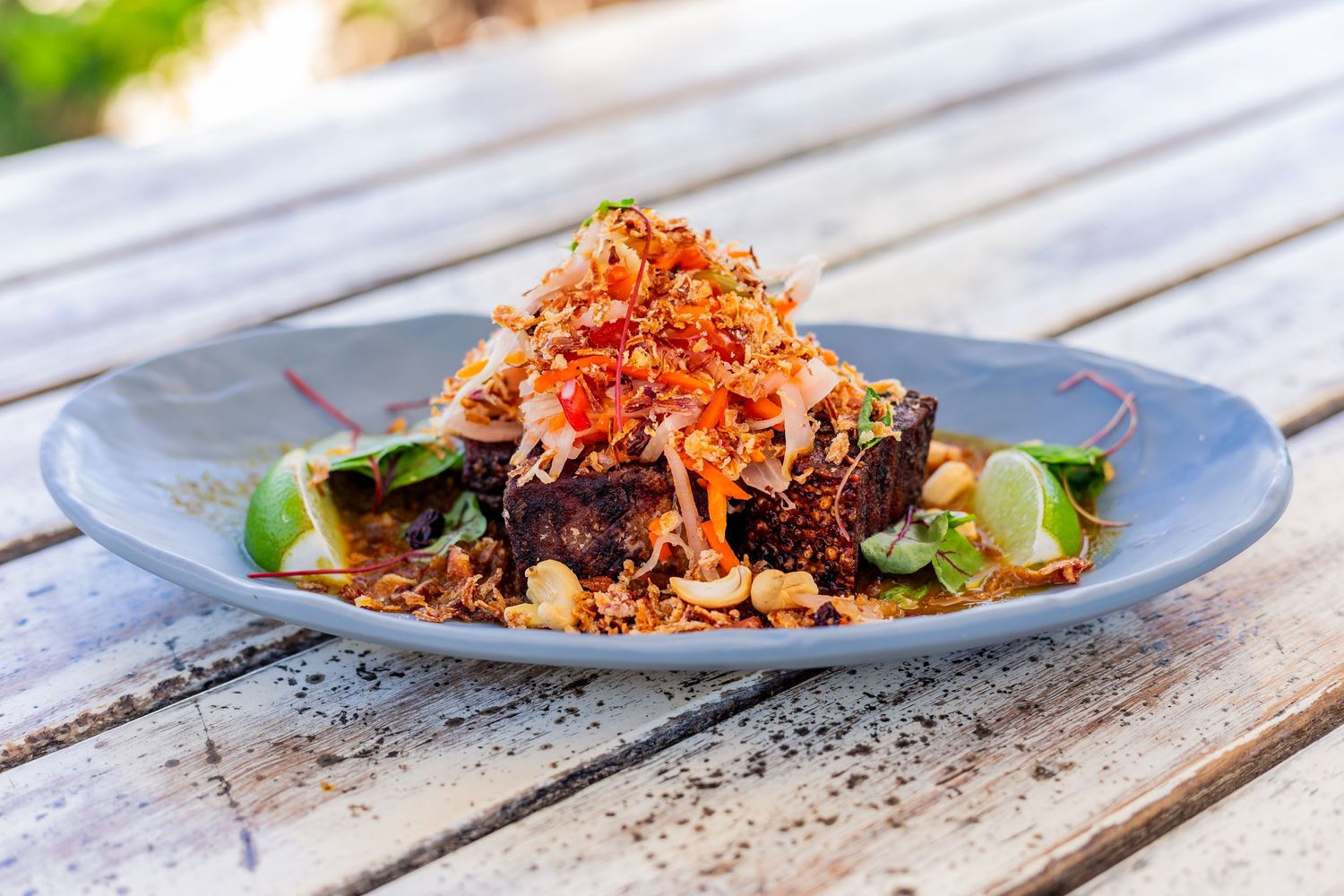 Asian-inspired dish with crispy toppings and greens served on a blue ceramic plate.