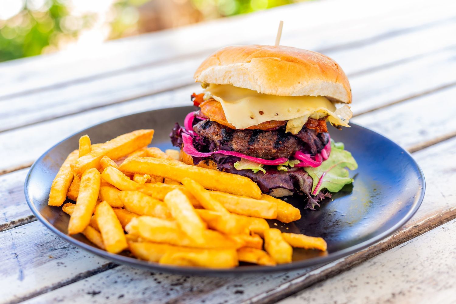 Gourmet burger with red cabbage slaw and golden french fries on a dark plate.