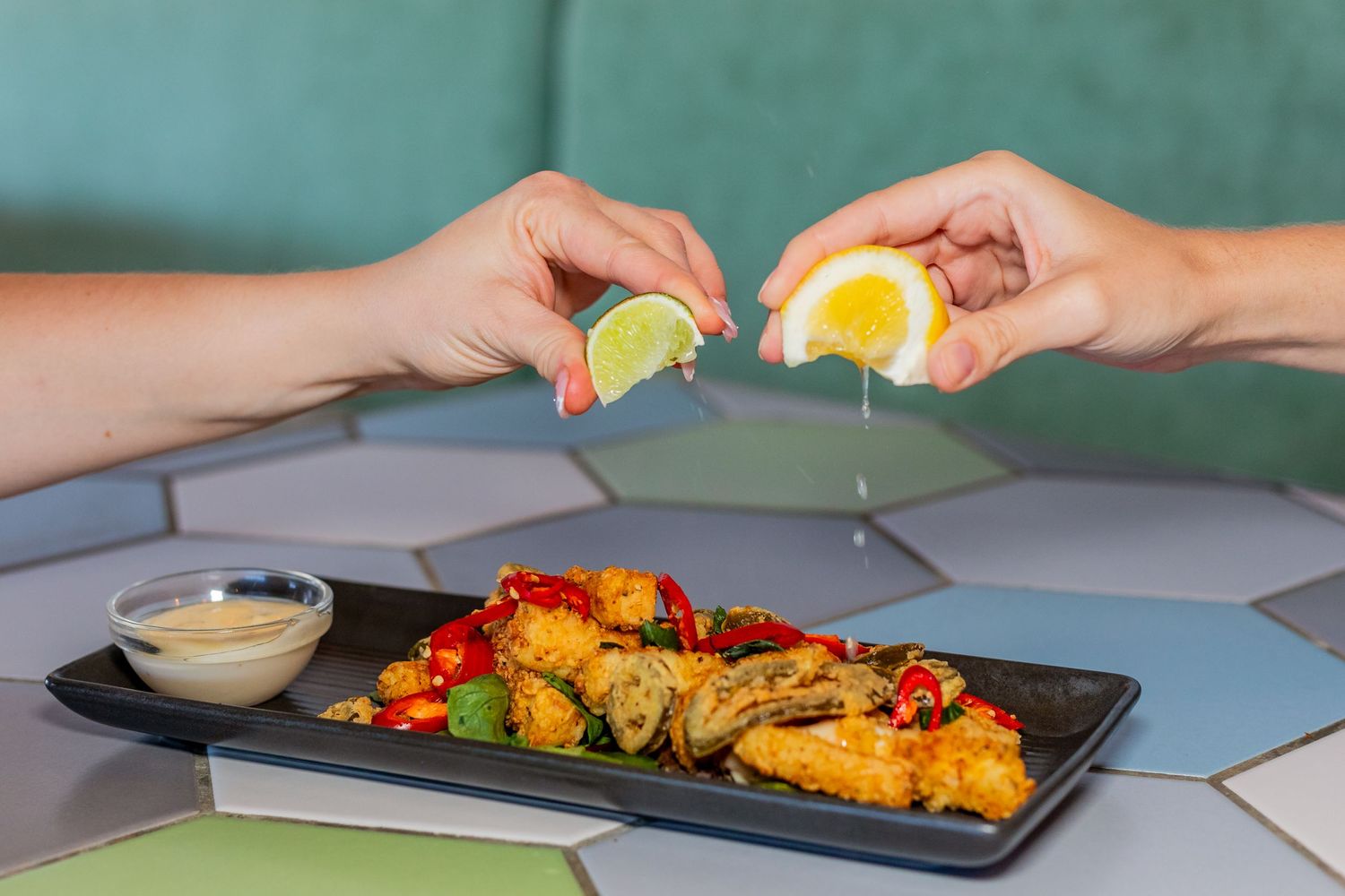 Seafood platter with fried fish and shrimp being garnished with fresh lemon wedges.