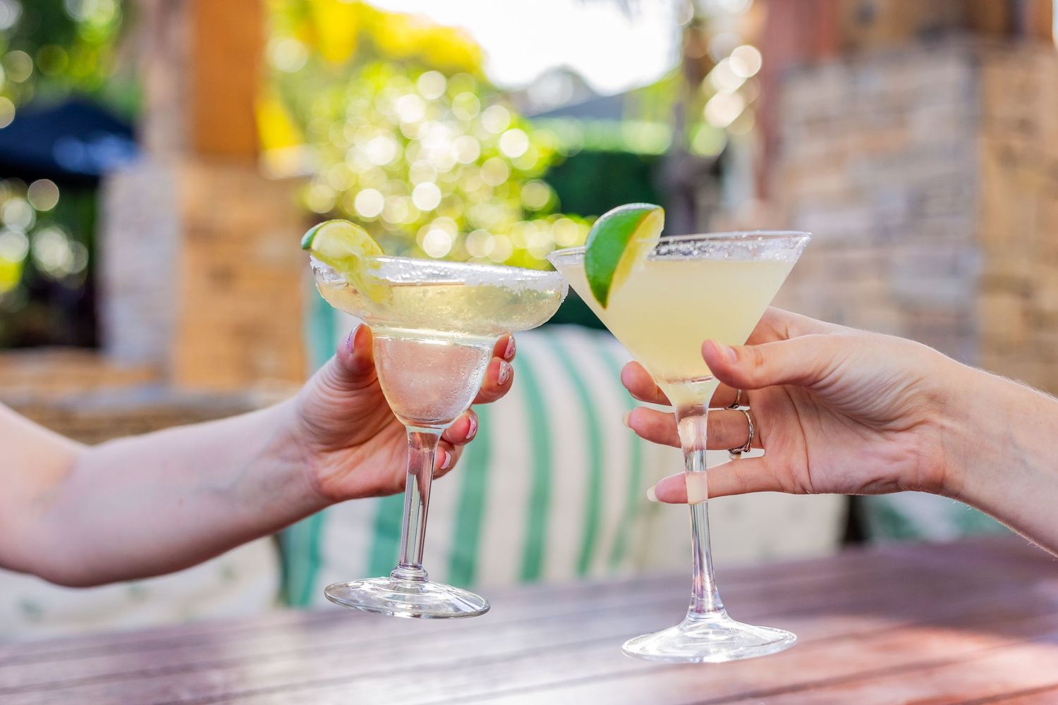 Two margarita cocktails garnished with lime being toasted outdoors.