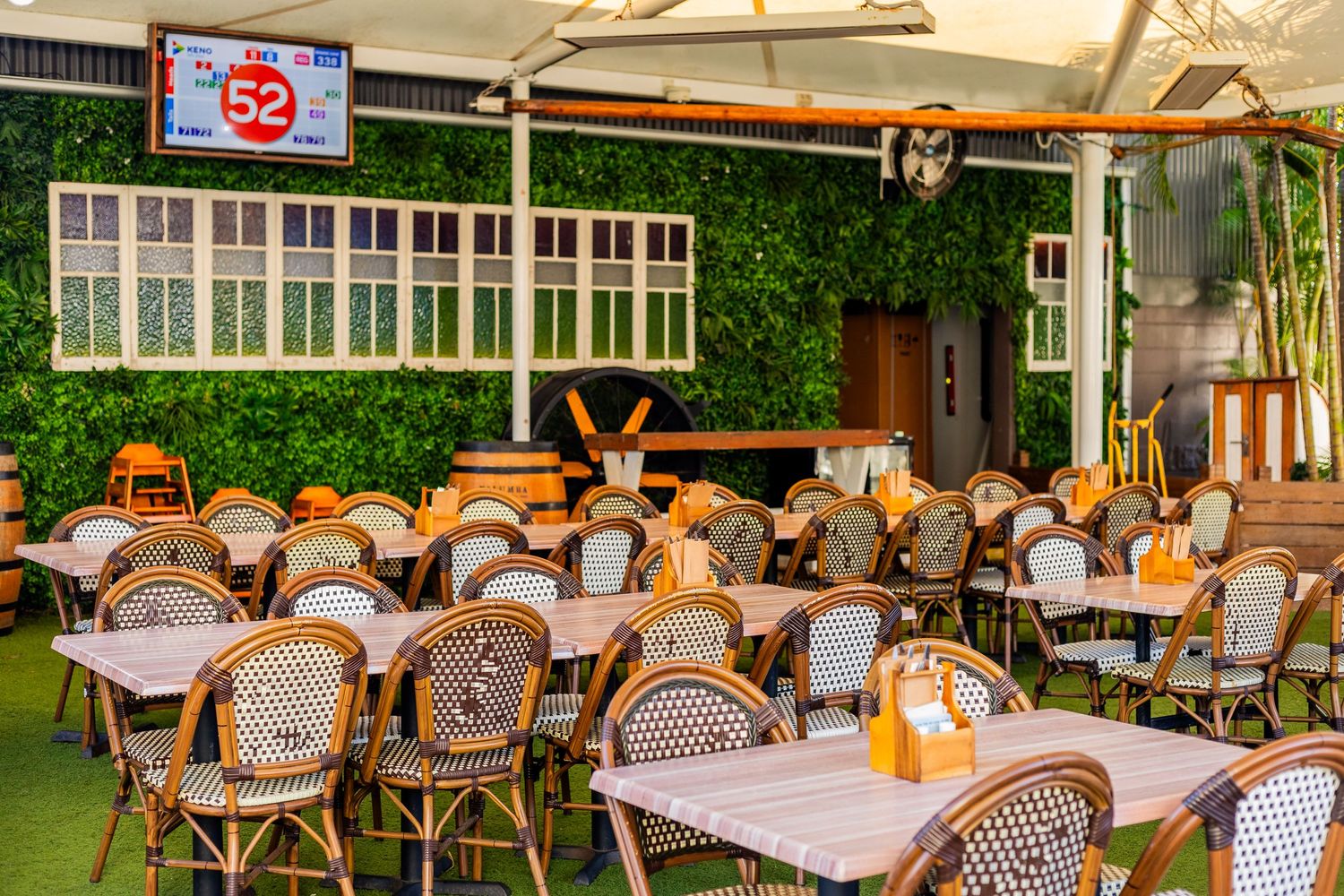 Outdoor restaurant patio with rattan chairs and checkered tablecloths under string lights.