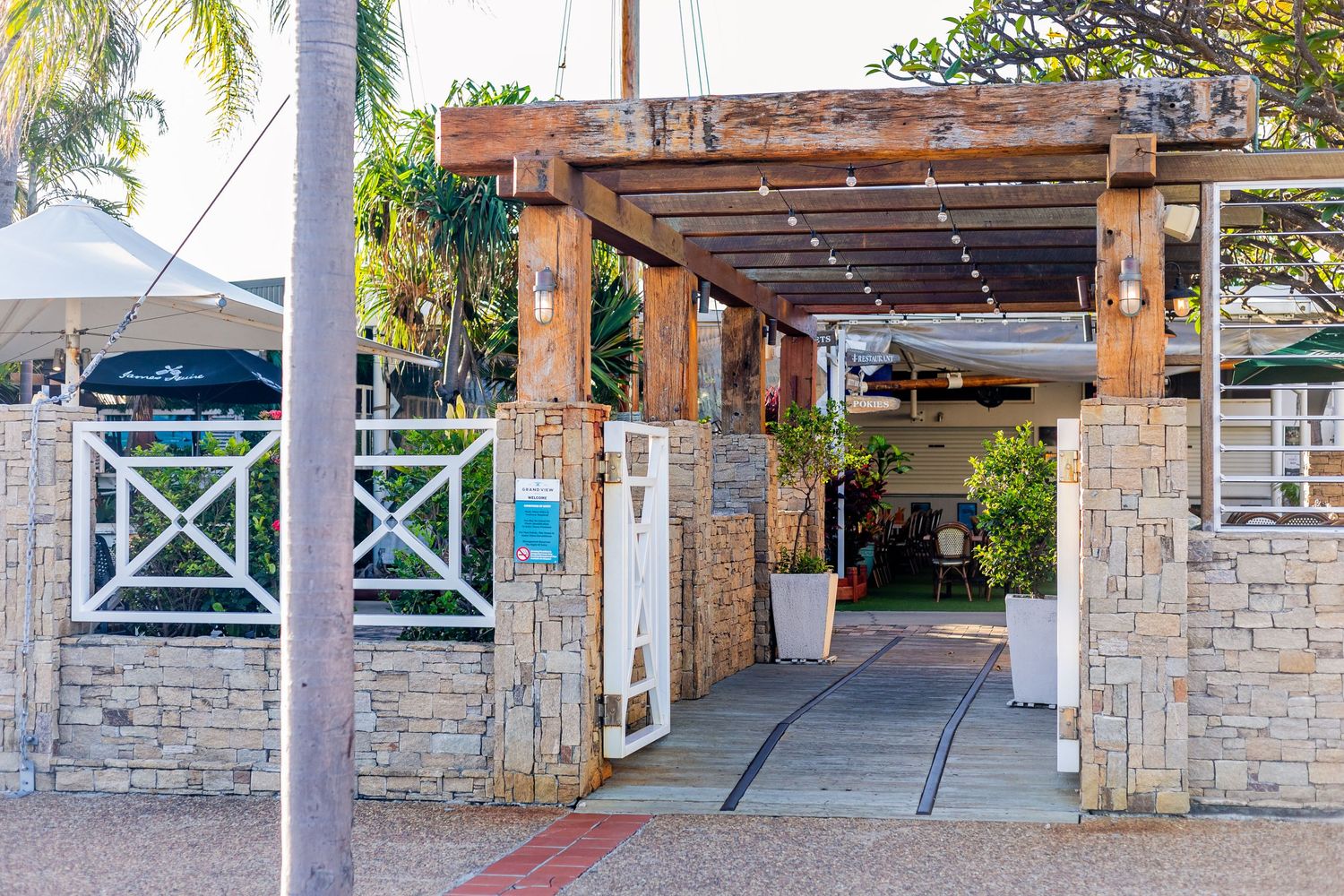 Stone entrance walkway with wooden pergola and tropical landscaping.
