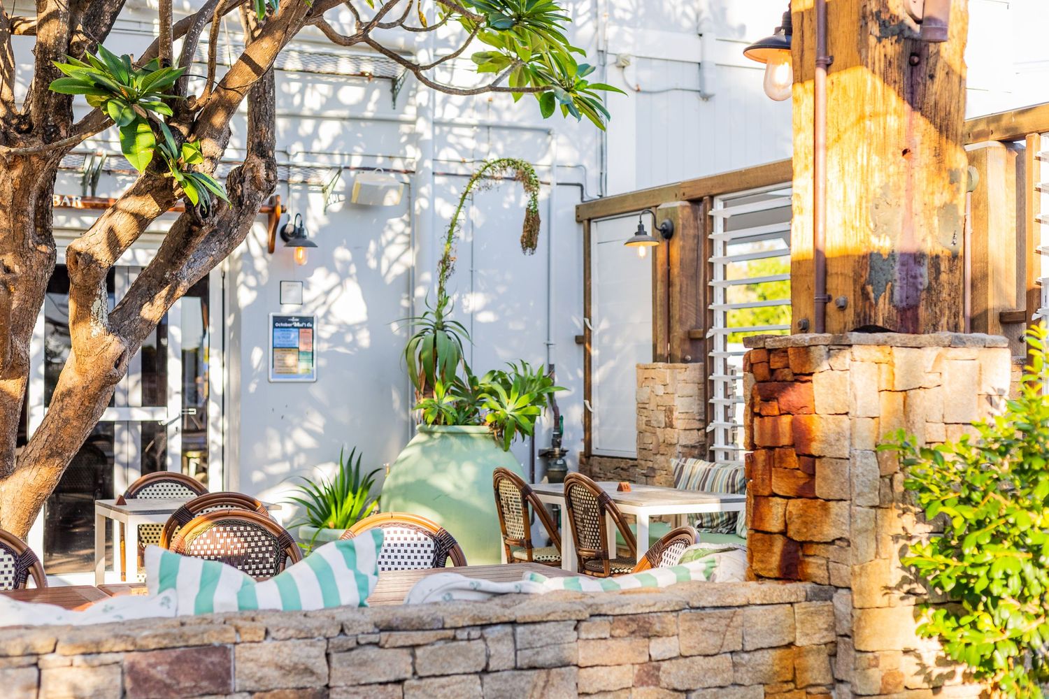 Rustic stone wall patio with white building and tropical plants in natural light.