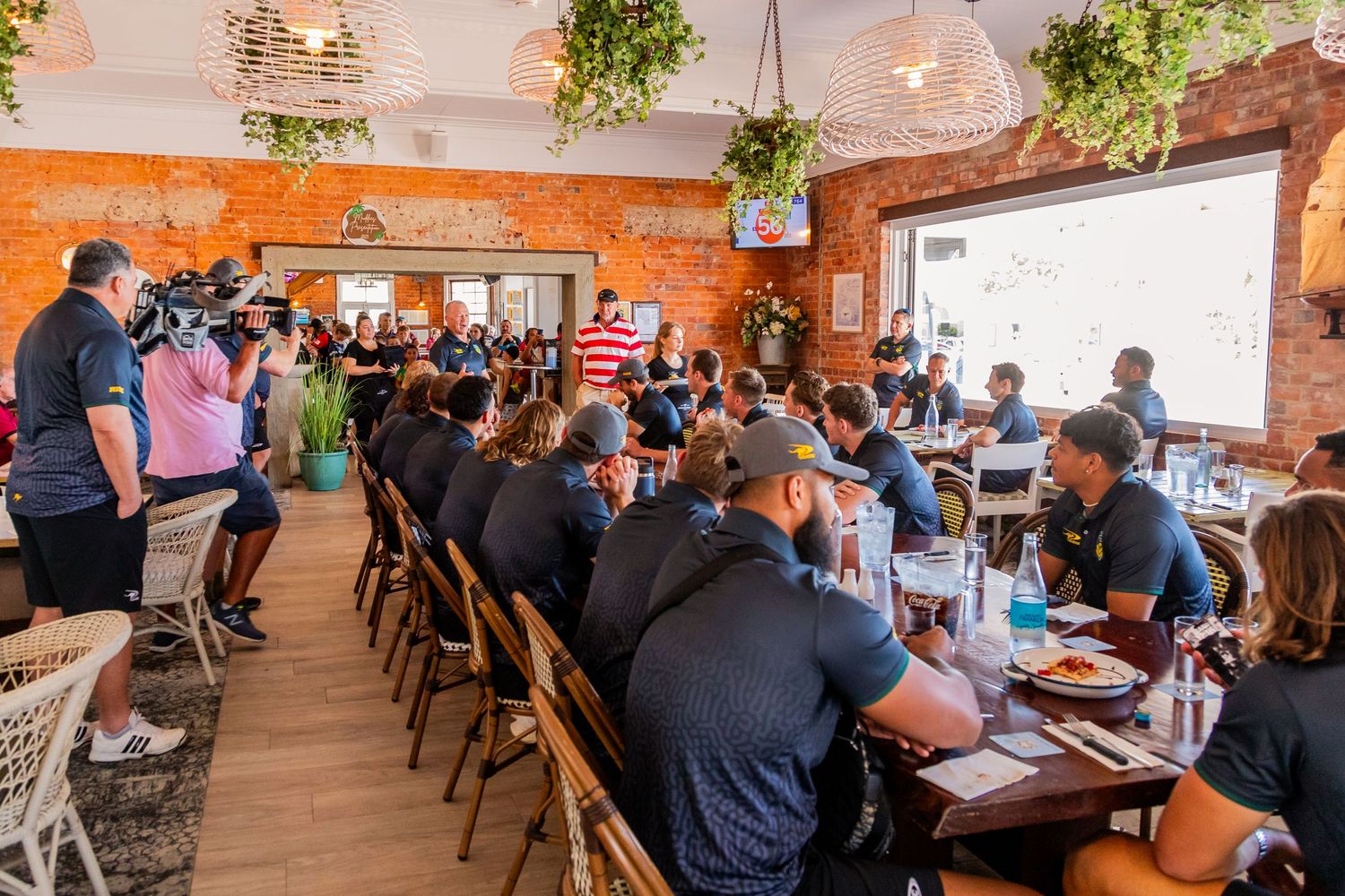 Busy restaurant interior with exposed brick walls and hanging plants during service.