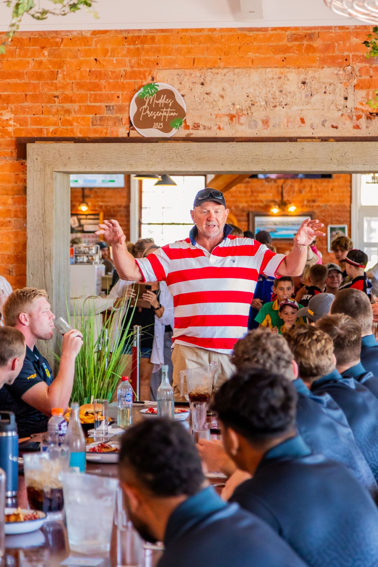 Crowded restaurant dining room with orange brick walls and enthusiastic atmosphere.
