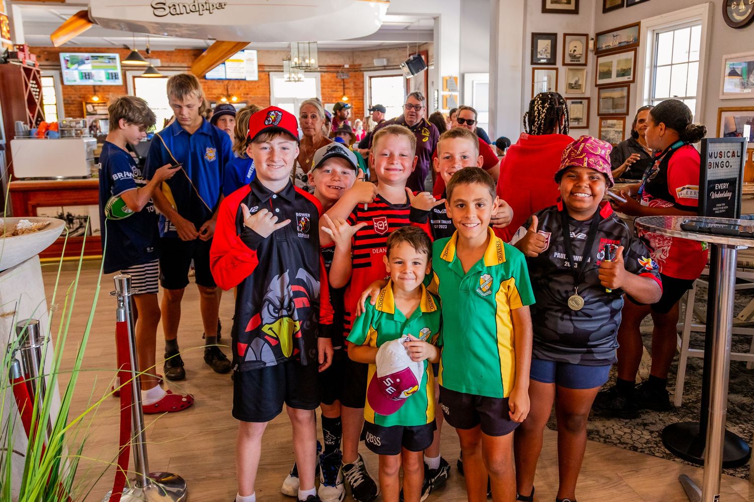 A group of young sports fans gather inside a casual restaurant wearing team jerseys and athletic gear.