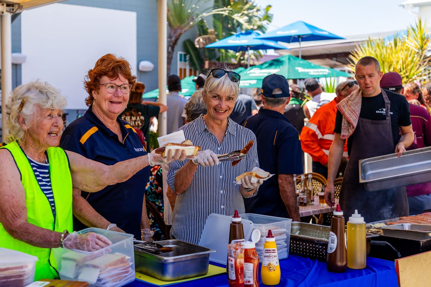 Volunteers working at an outdoor food service station with cooking equipment and condiments.