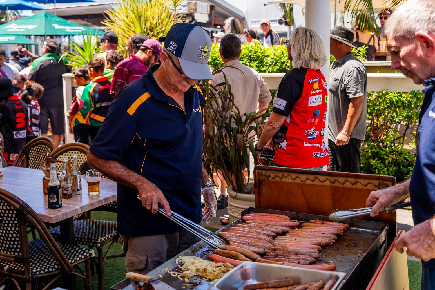 Person grilling hot dogs and sausages at an outdoor community event.