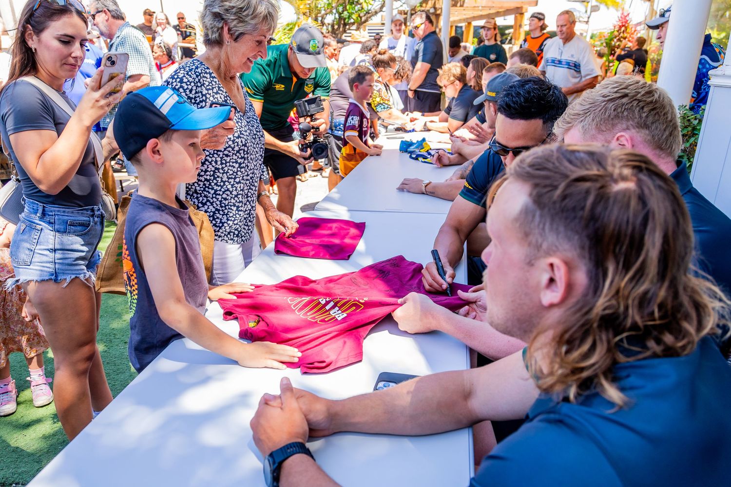 Fans getting autographs at a signing table during an outdoor event.