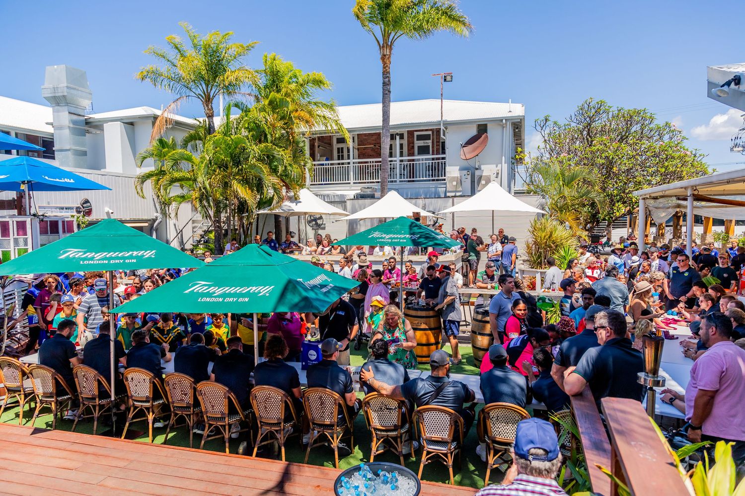 Aerial view of crowded outdoor restaurant patio with turquoise umbrellas and tropical landscaping.