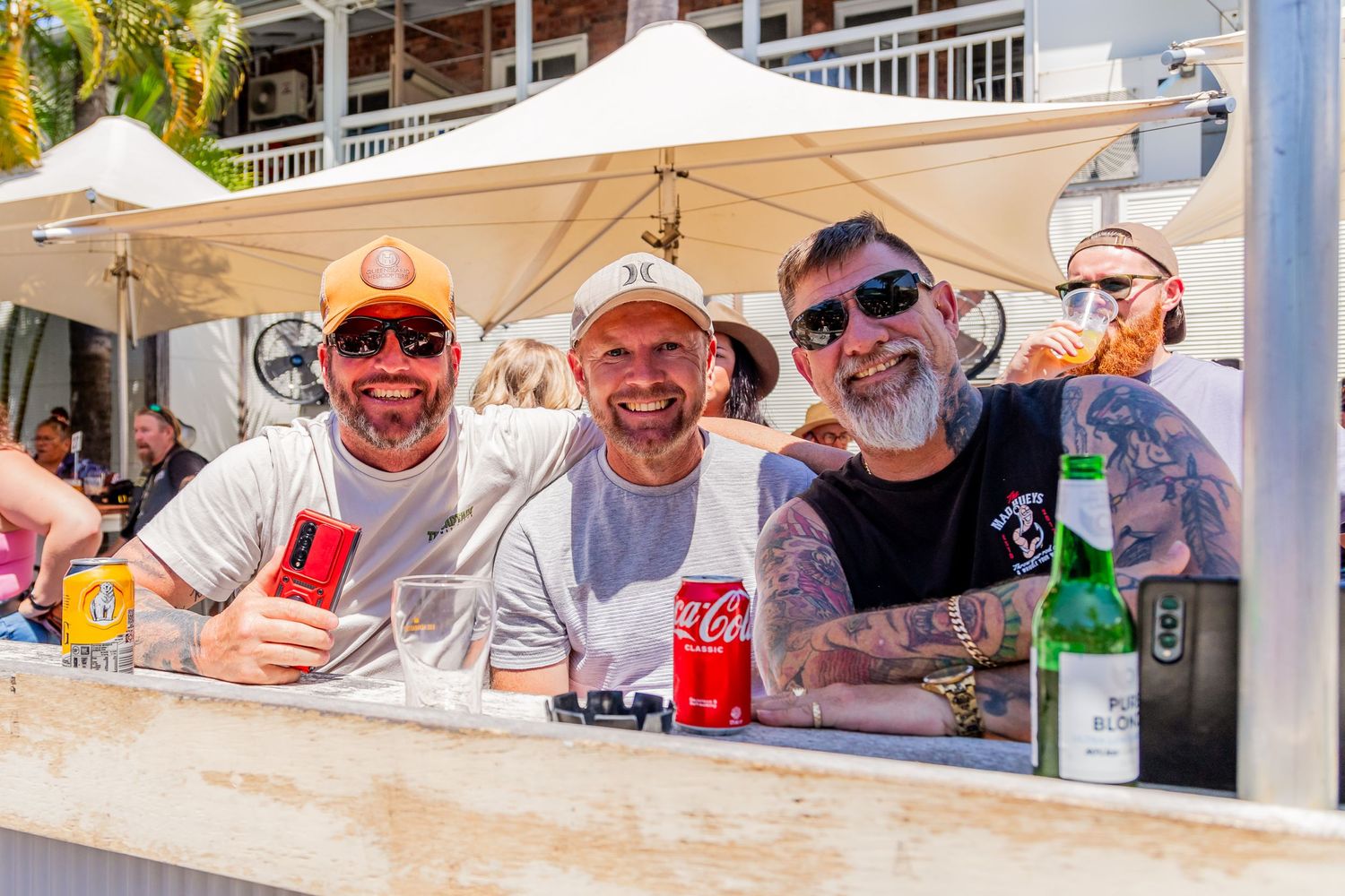 Three friends enjoying drinks together at an outdoor bar counter.