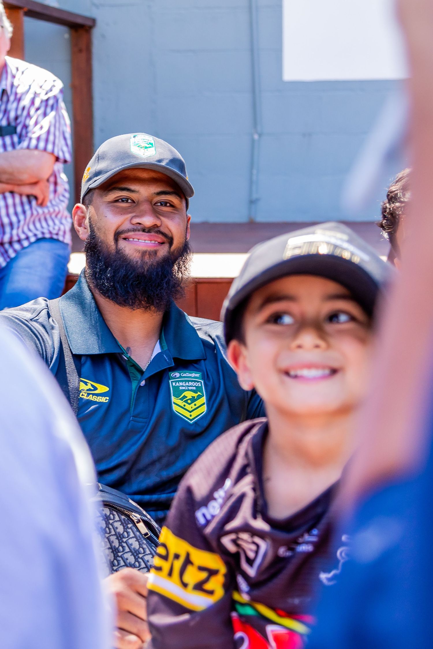 A rugby league fan poses with a young supporter wearing team merchandise at a sports event.