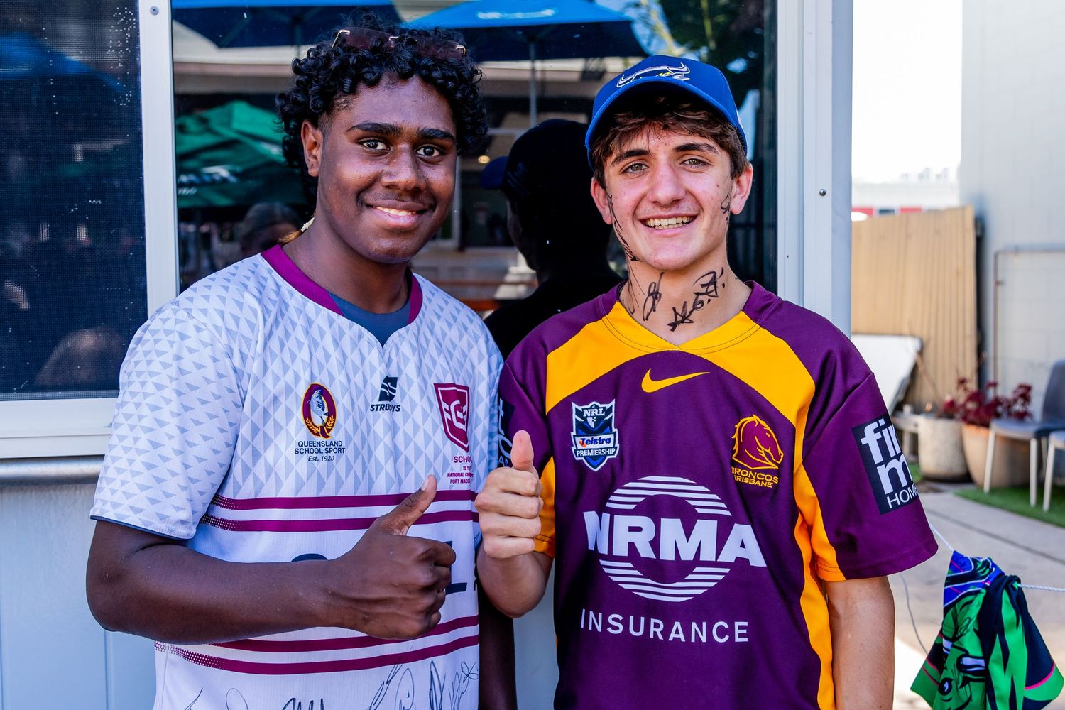 Two young sports fans in different team jerseys pose together at an event.