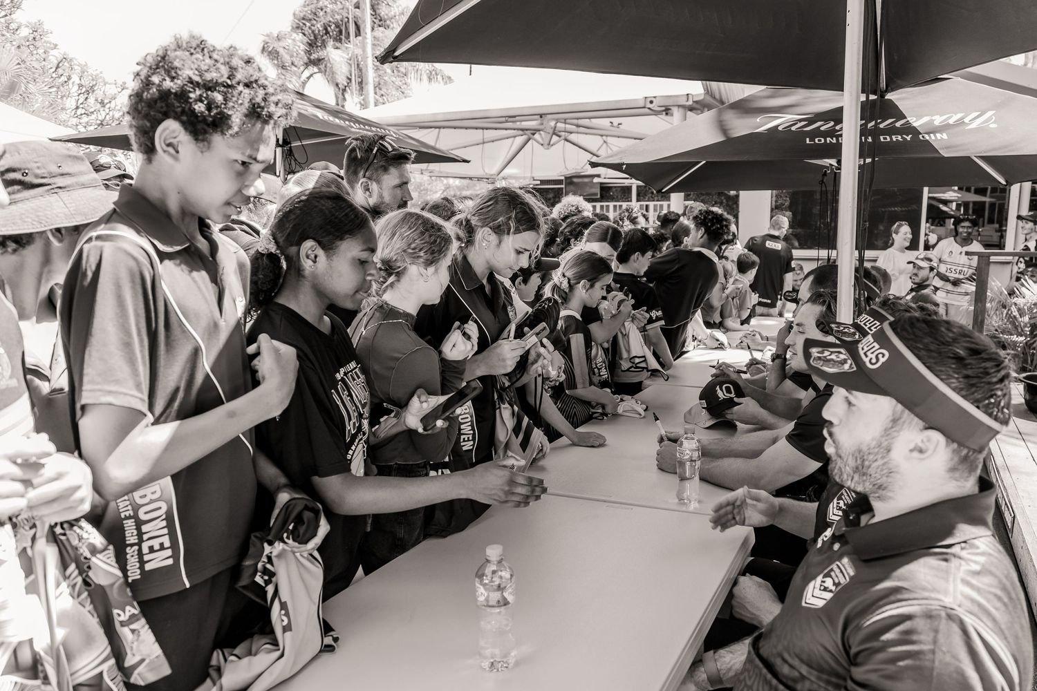 People lined up at an outdoor signing table during a fan meet and greet event.