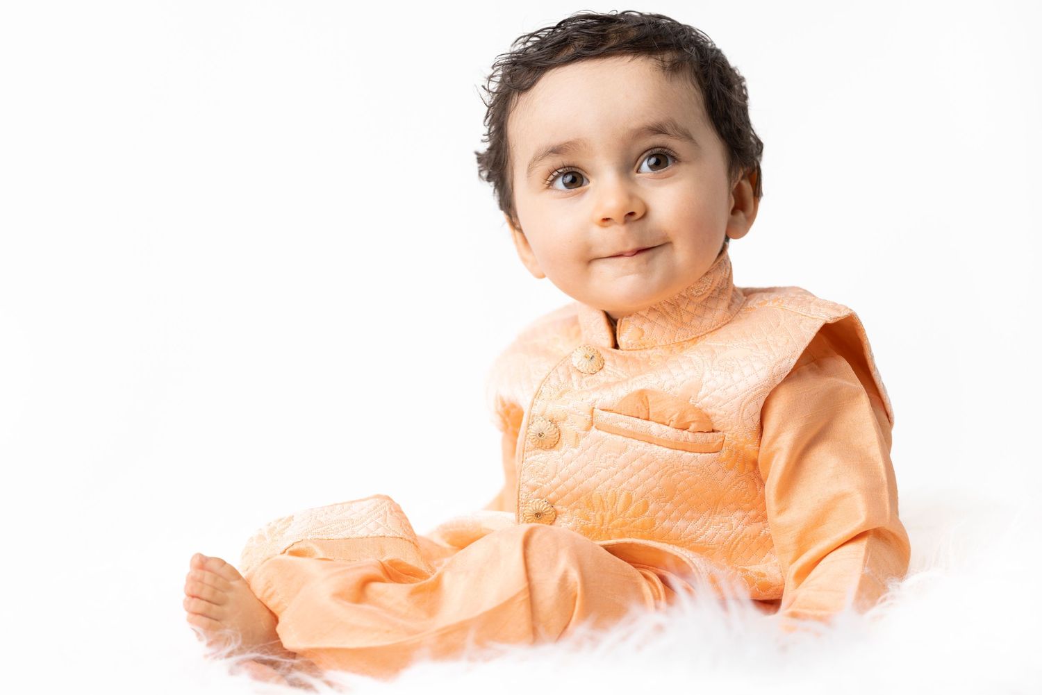 Baby wearing peach colored outfit sitting against white background.