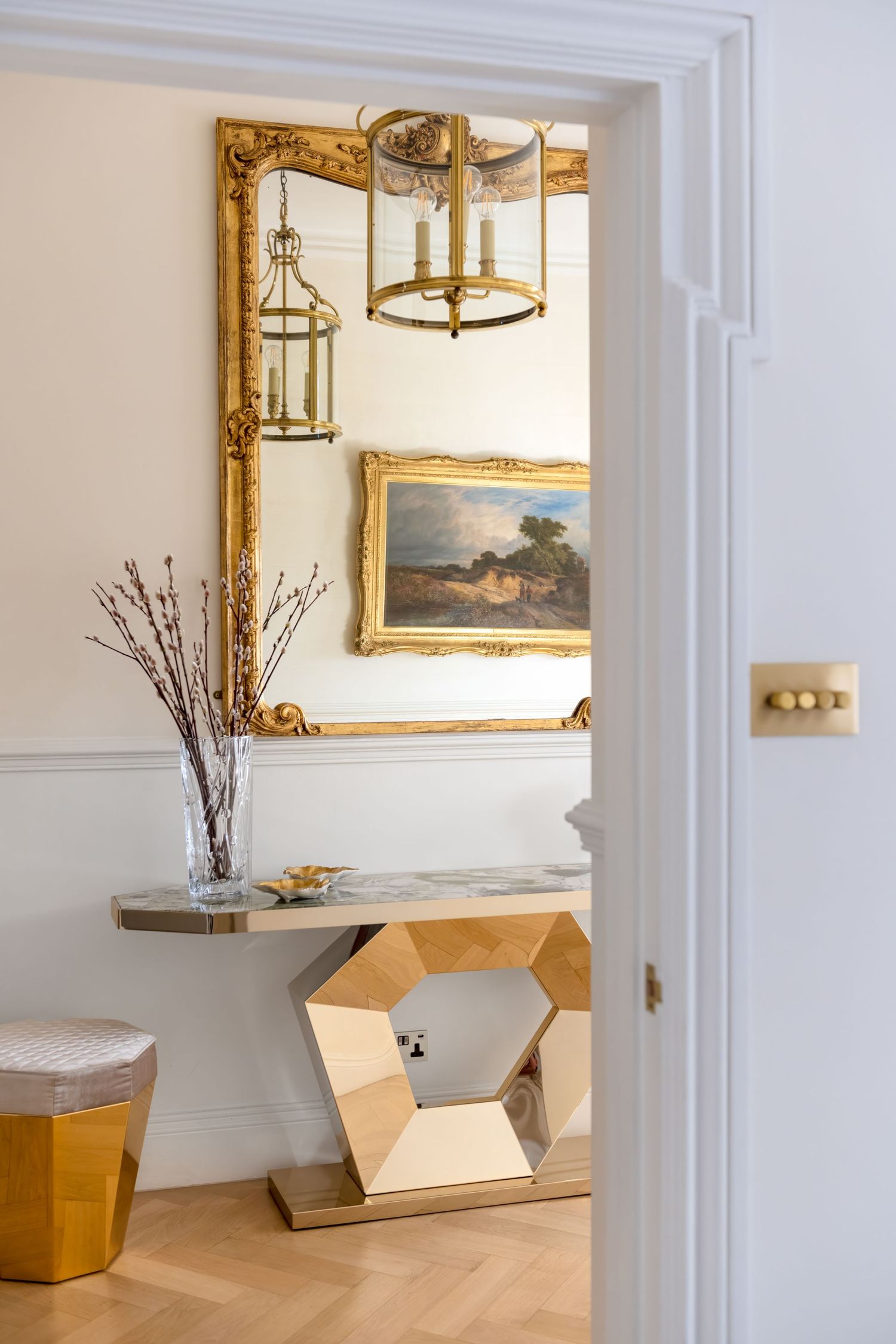 Hanging brass lantern reflected in gilded mirror with a gold console underneath in a London townhouse hallway