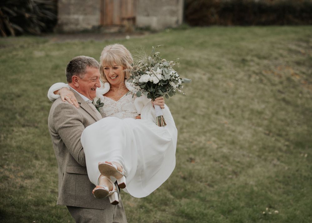 Groom carries bride across the garden at St Elizabeth's House, Plympton