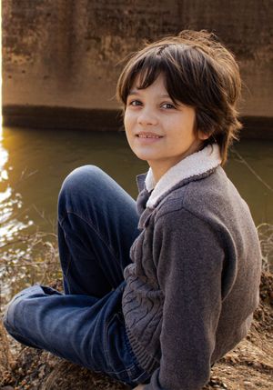 Young person in gray jacket sitting casually by water during golden hour.