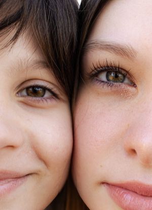 Two faces close together showing brown eyes and glowing skin in a macro beauty shot.