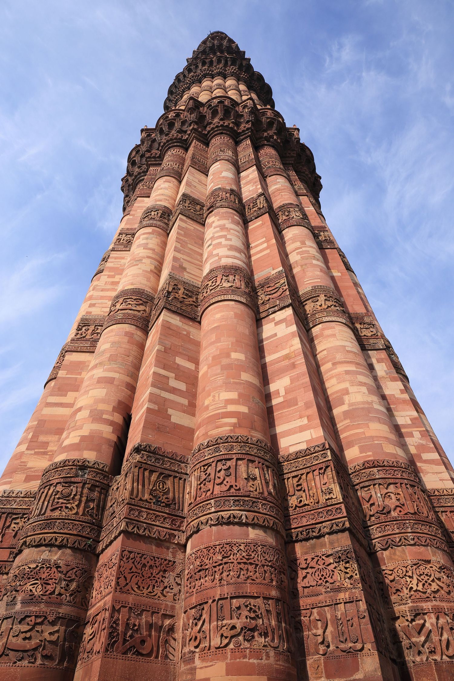 Towering Qutub Minar minaret showcasing detailed Islamic architecture against blue sky in Delhi.