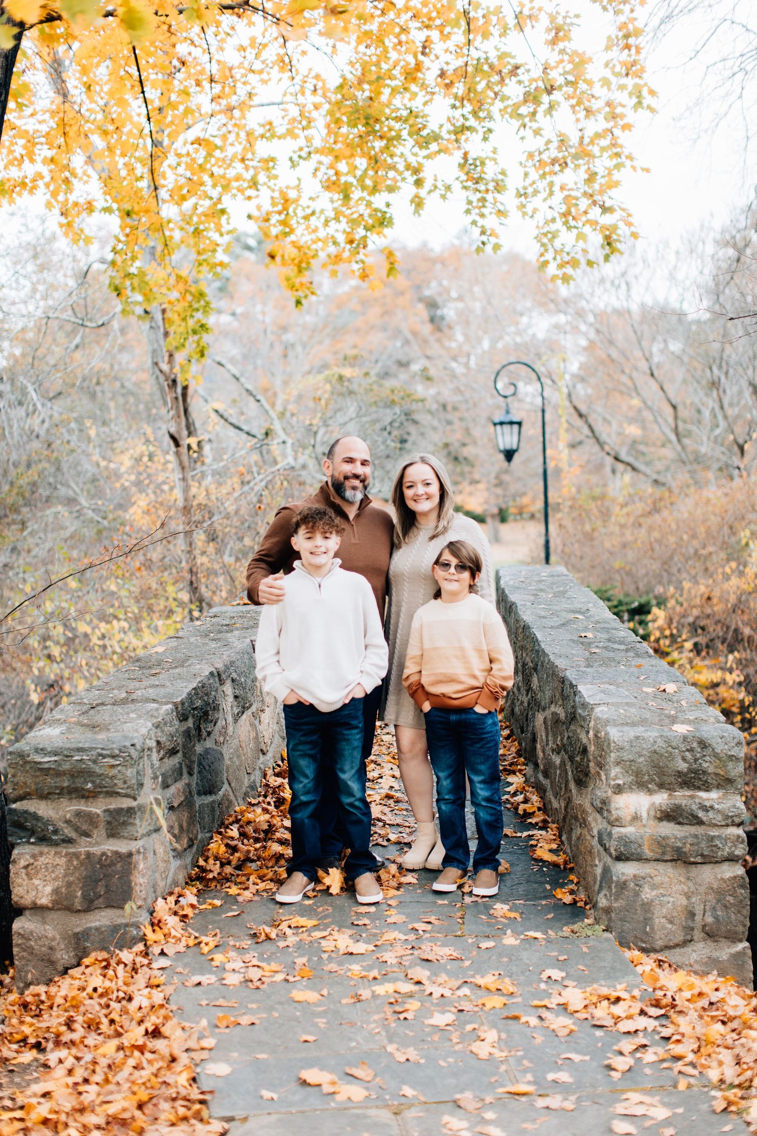 Family of four standing on stone bridge surrounded by fall foliage.