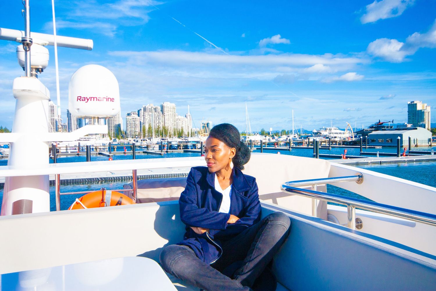 Person relaxing on yacht deck with blue sky and harbor views in background.