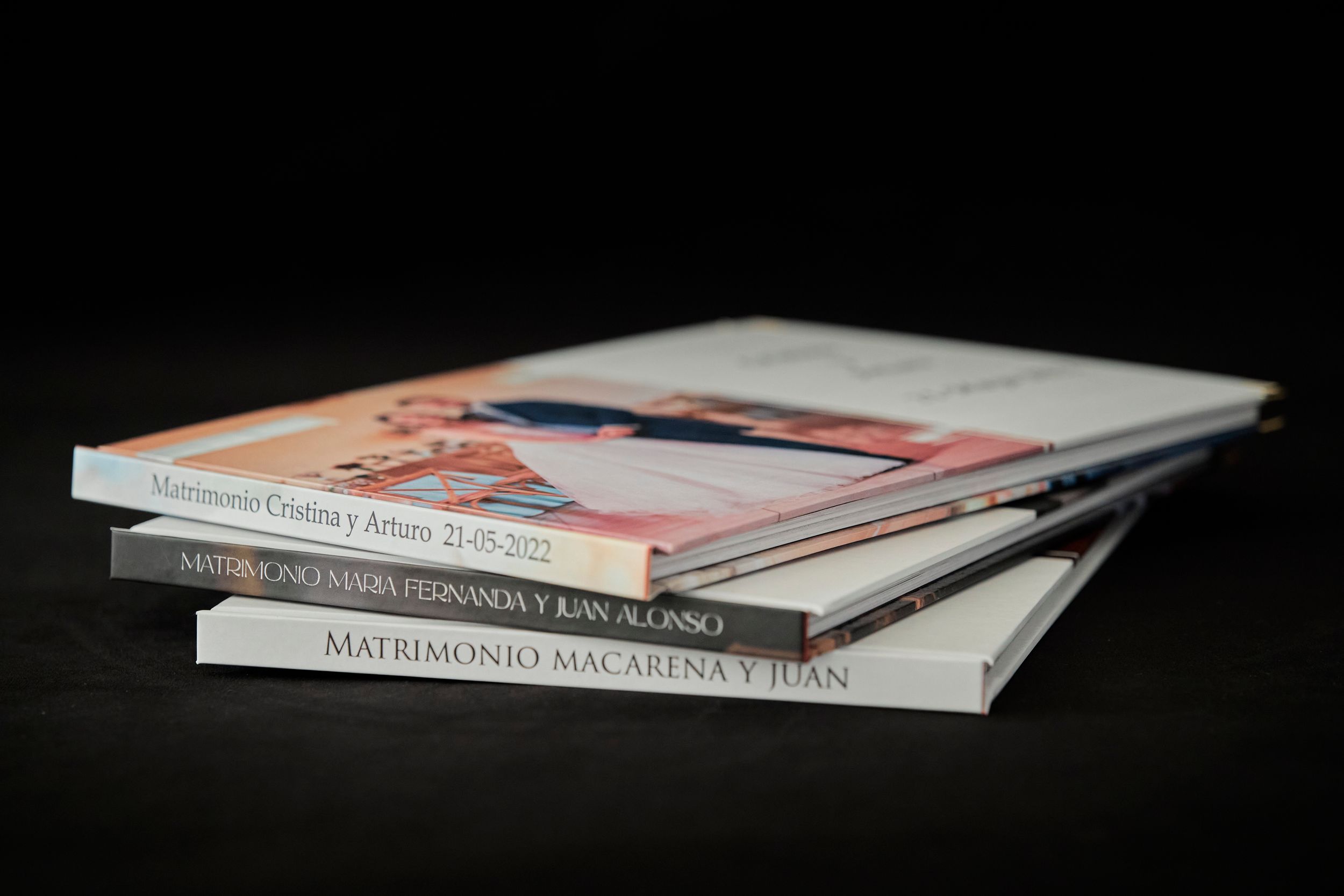 Stack of professional wedding photo albums on black surface.