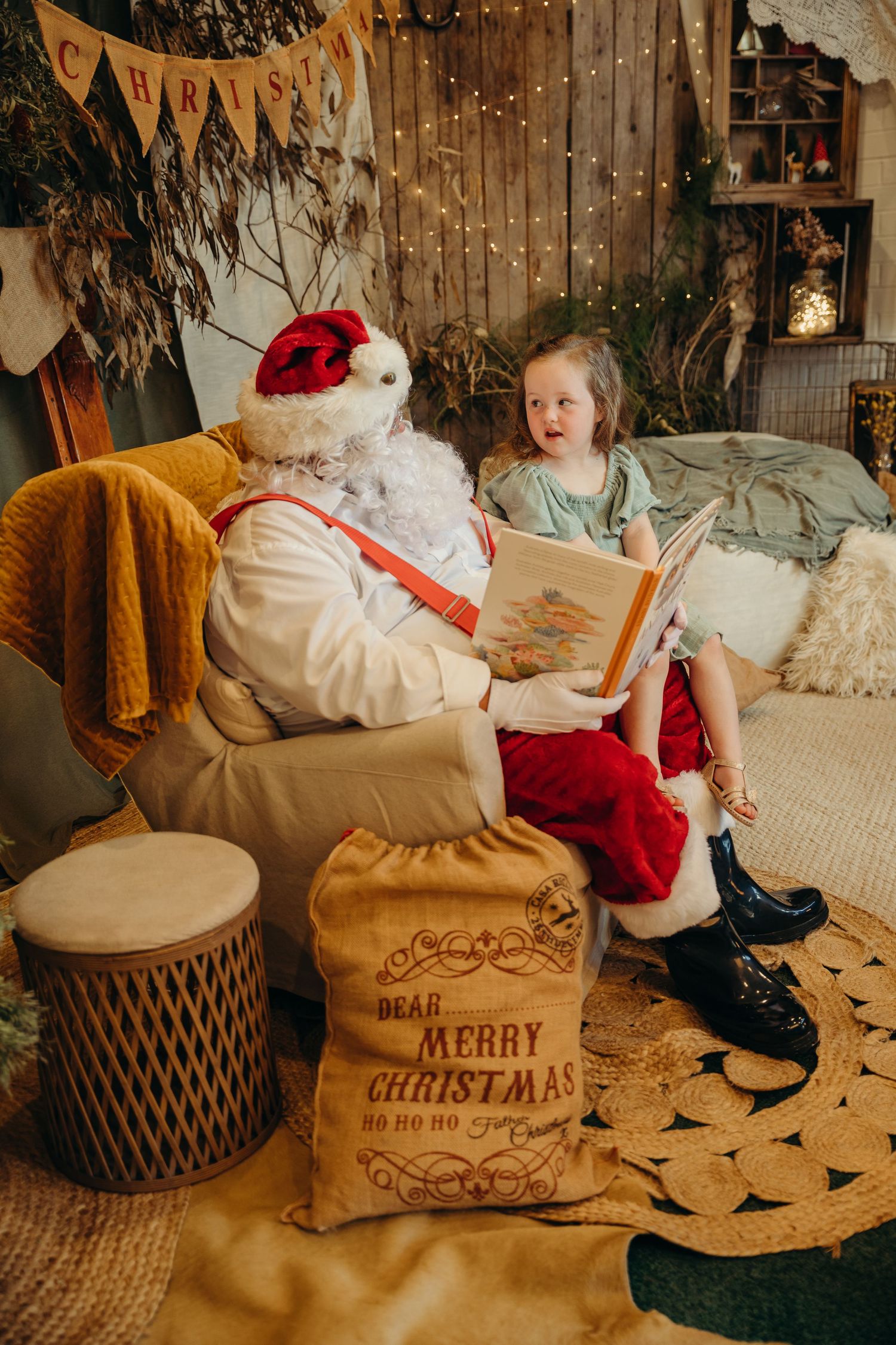 Excited little girl sitting with Santa Claus reading a Christmas storybook in a festive decorated room.
