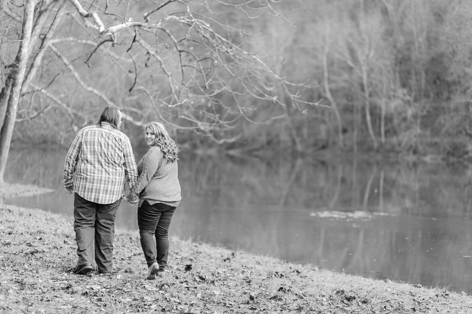 Black and white photo of a couple walking together in a natural outdoor setting by a lake.