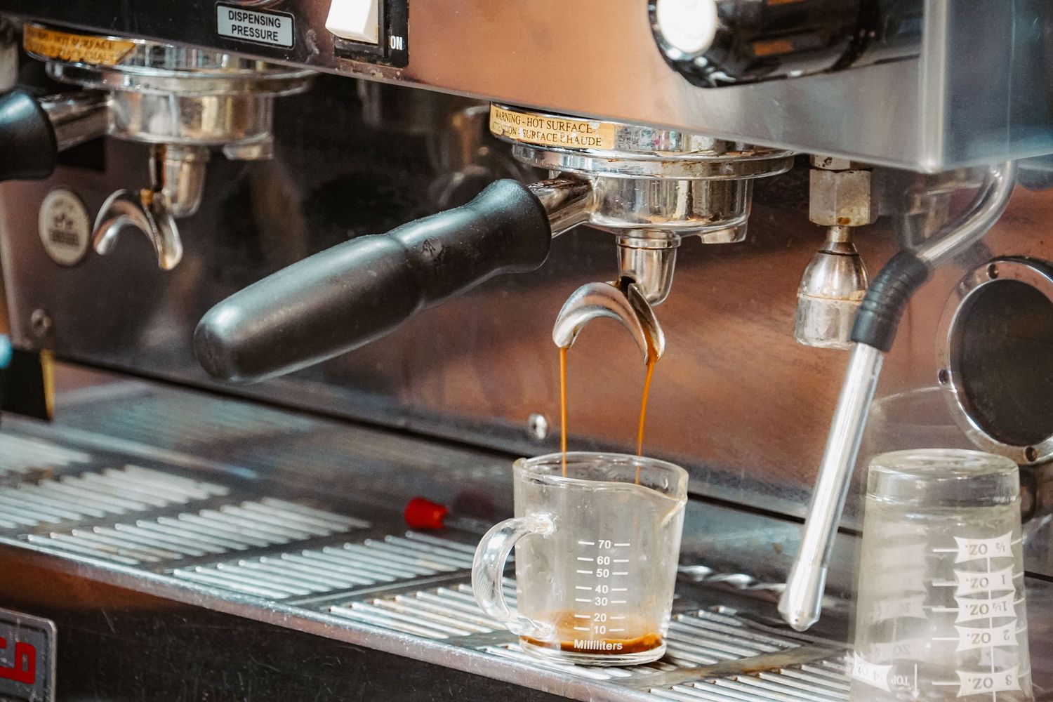 Espresso machine brewing fresh coffee into a glass measuring cup.