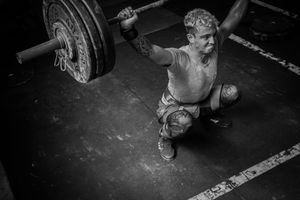 Black and white photo of weightlifter performing overhead snatch lift in gym setting.