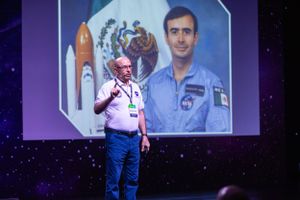 Speaker presents on stage with space-themed projection backdrop.