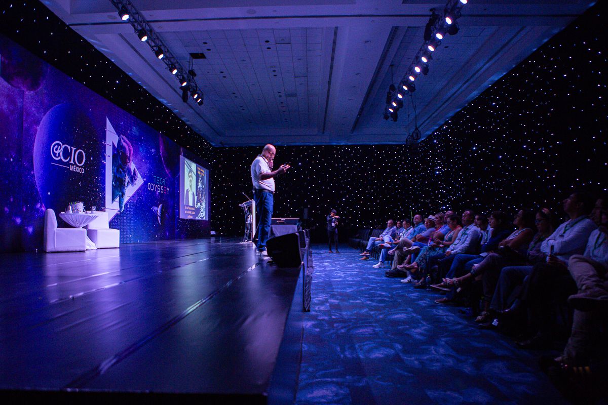 A performer on stage addresses an audience in a darkened theater with starlit backdrop.